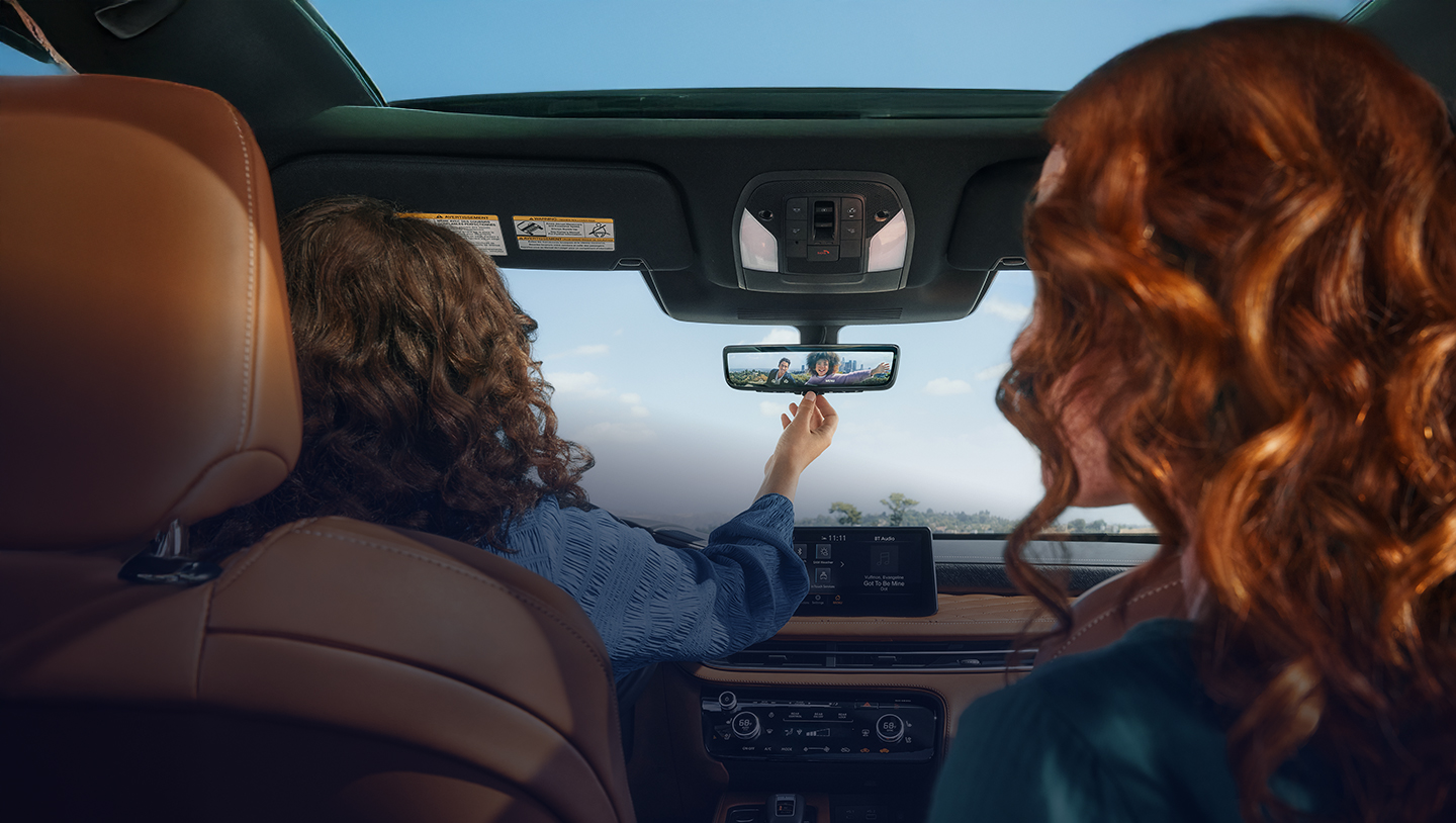 Dos mujeres en la cabina de su QX60 usando el espejo inteligente