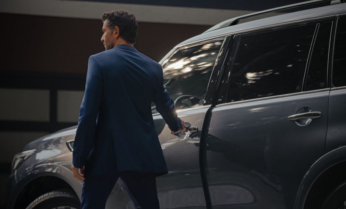 Friends walking to a 2024 INFINITI QX80 SUV parked in front of a building at night.