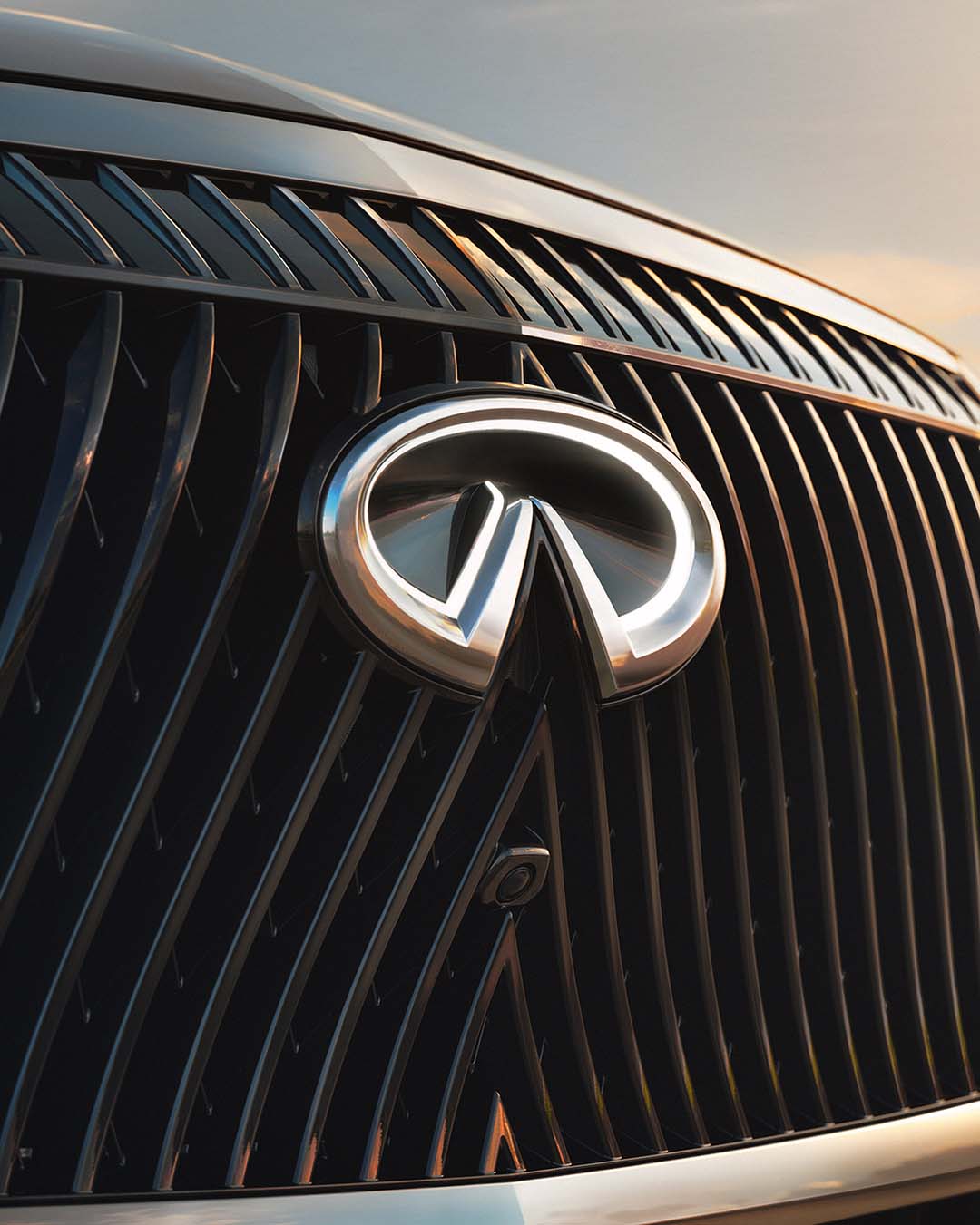 Angled grille view of INFINITI badge with polished vertical elements in natural light