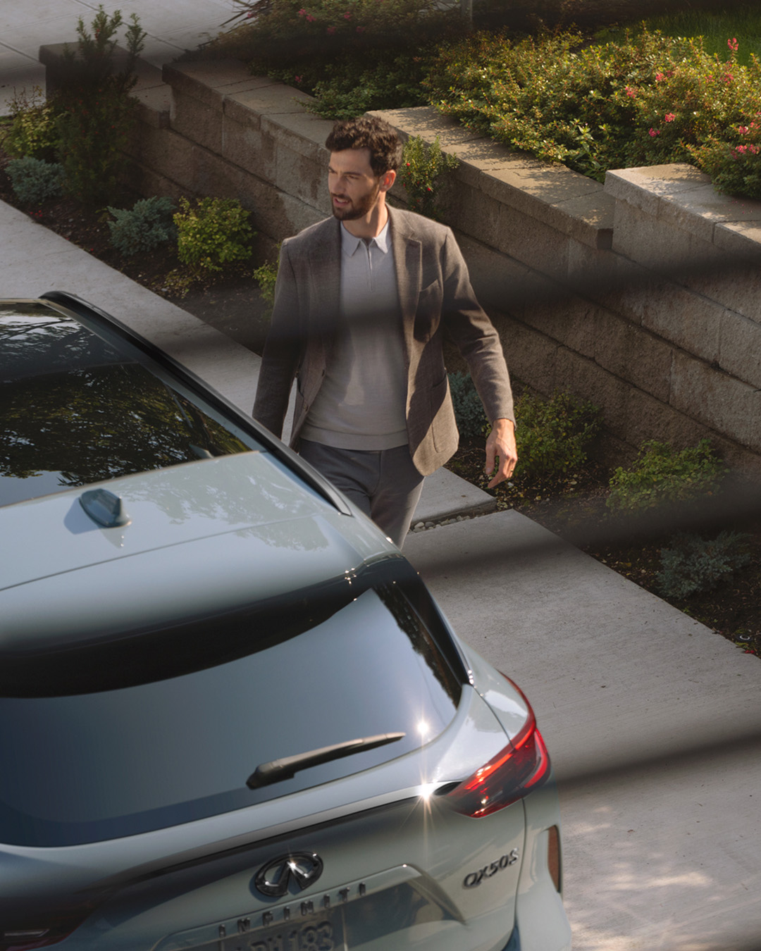 View of owner walking past INFINITI QX50 through window blinds 