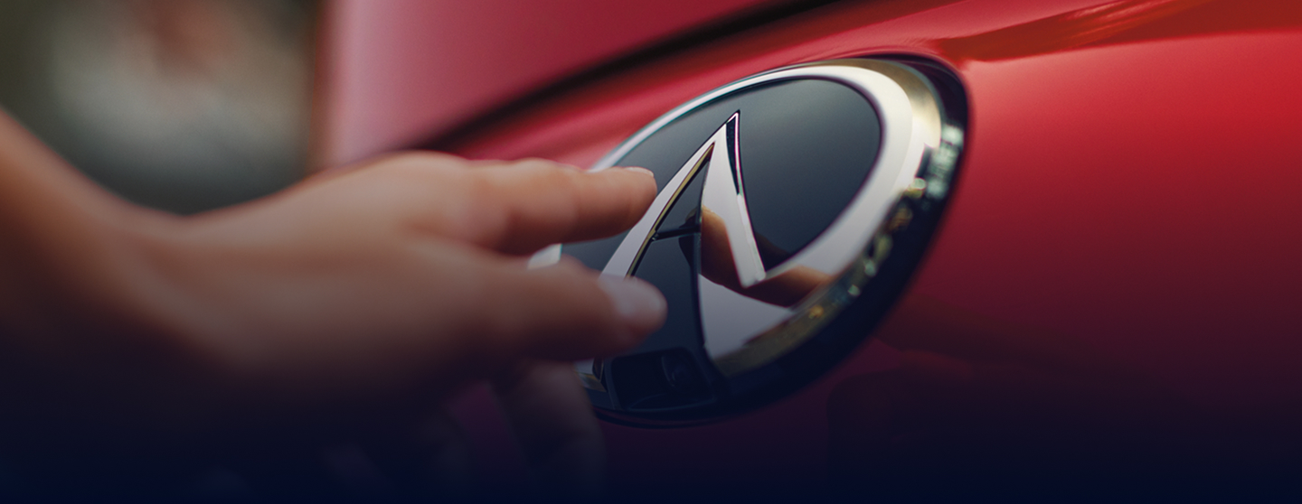Close-up of 2025 INFINITI QX55 rear badge with hand reaching toward INFINITI emblem