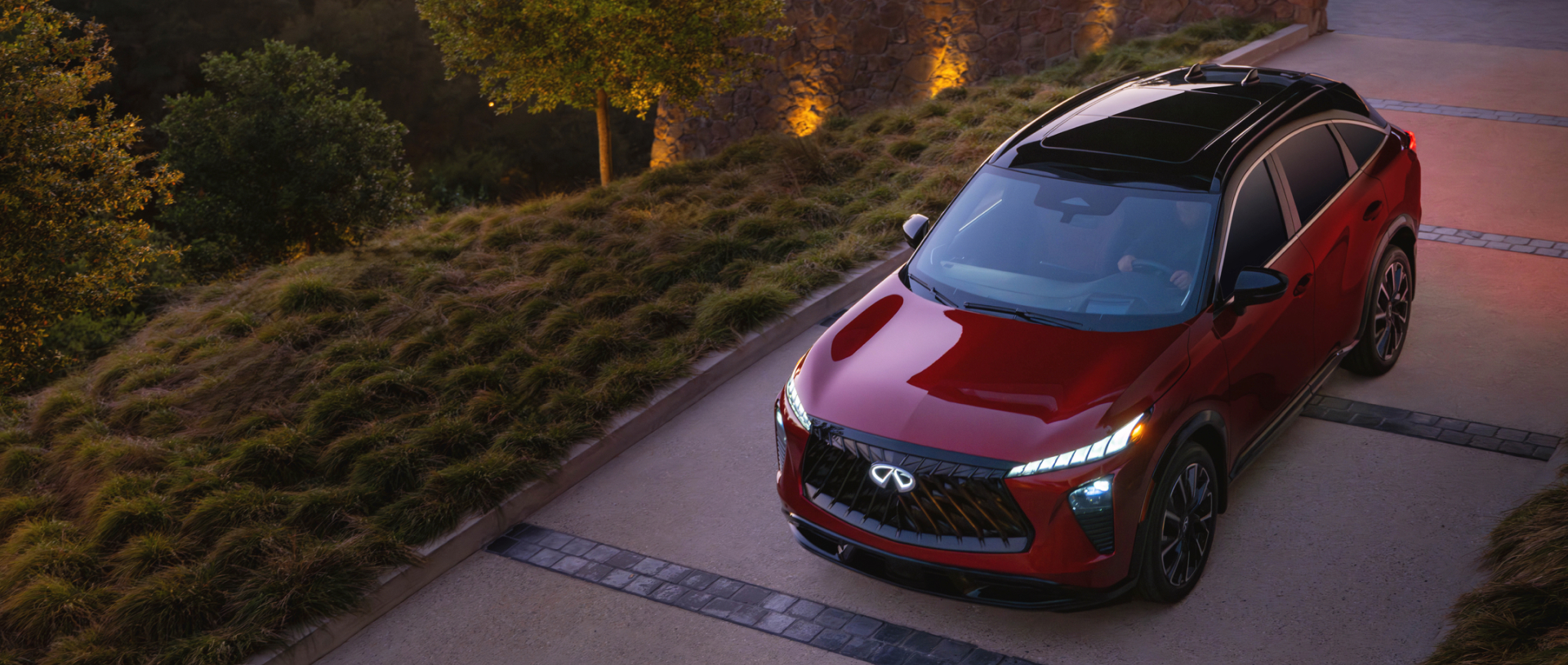 Red INFINITI QX65 driving onto driveway at night