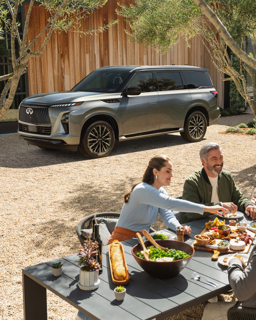 Family having backyard meal in front of their INFINITI QX80