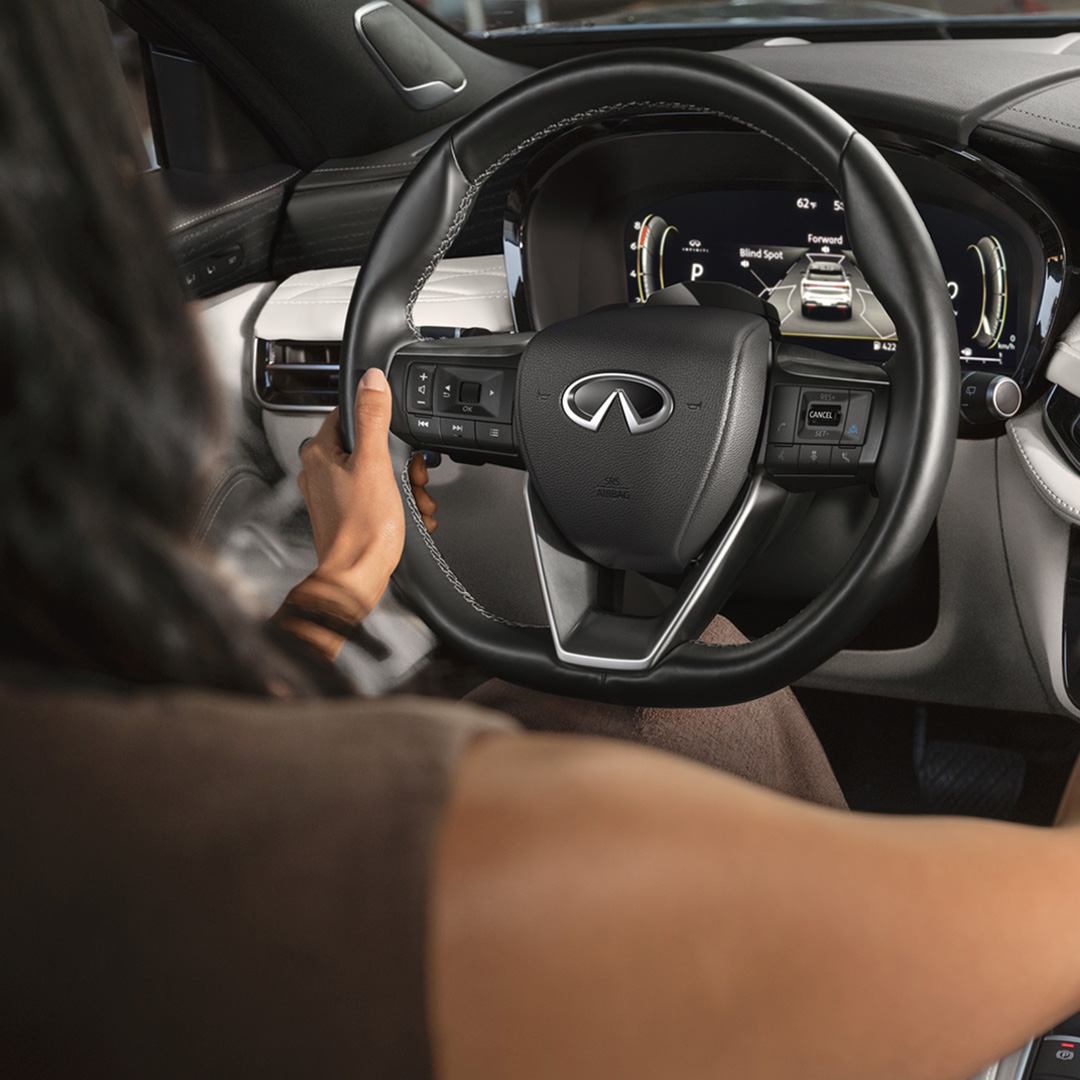Driver behind wheel of 2027 INFINITI QX60 viewing instrument cluster with active driver assist features