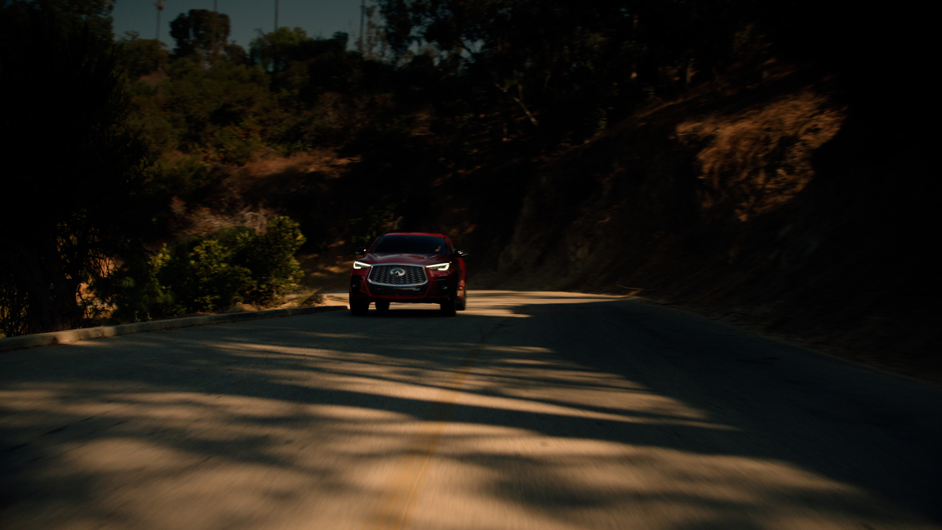Red INFINITI QX55 luxury crossover coupe driving on a winding canyon road