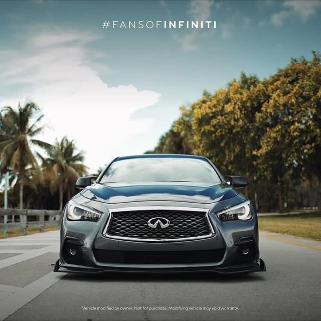 Black INFINITI Q50 facing camera with palm trees and cloudy sky