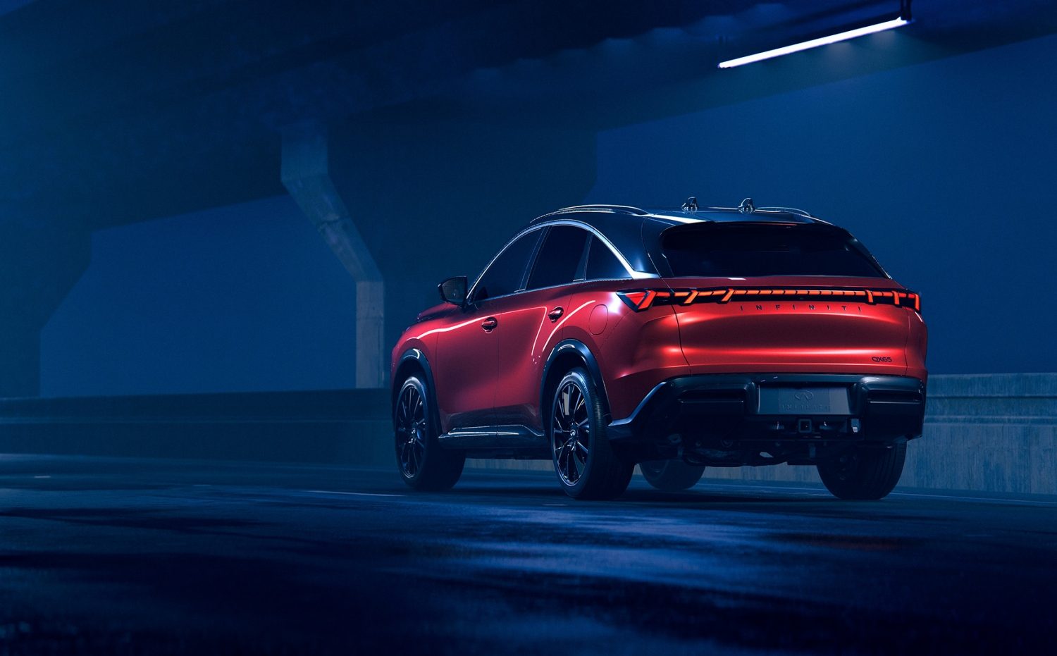 Rear three-quarter view of the 2027 INFINITI QX65 illuminated in an urban setting