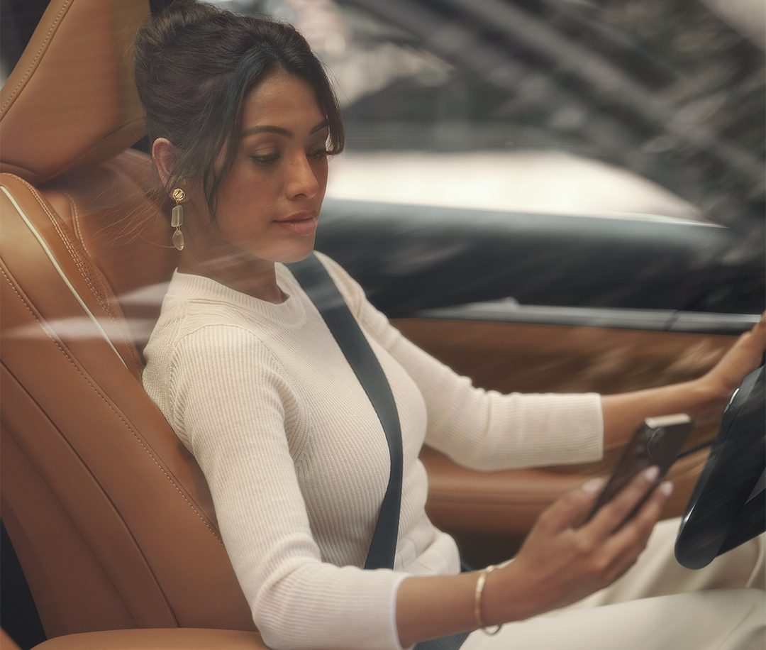 Mujer sentada en su INFINITI QX60 usando su celular