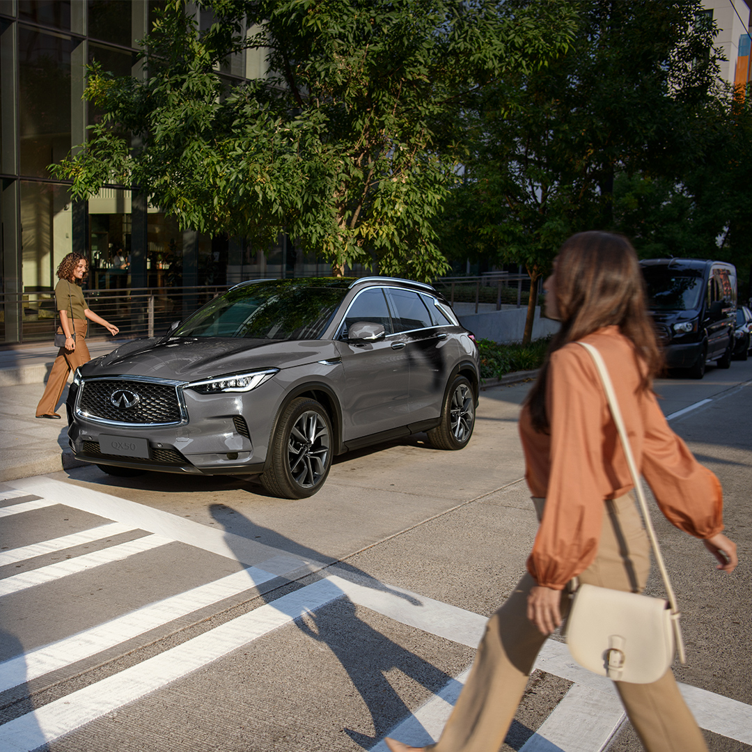 Mujer cruzando la calle, observando un QX50 estacionado