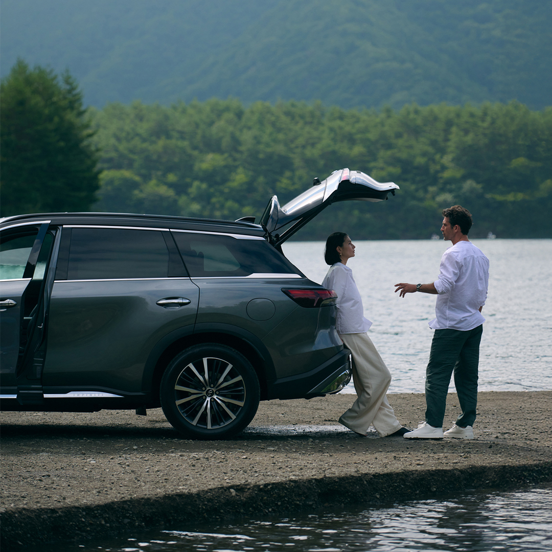 Hombre y mujer disfrutando de la tarde frente a un lago, junto a su QX60