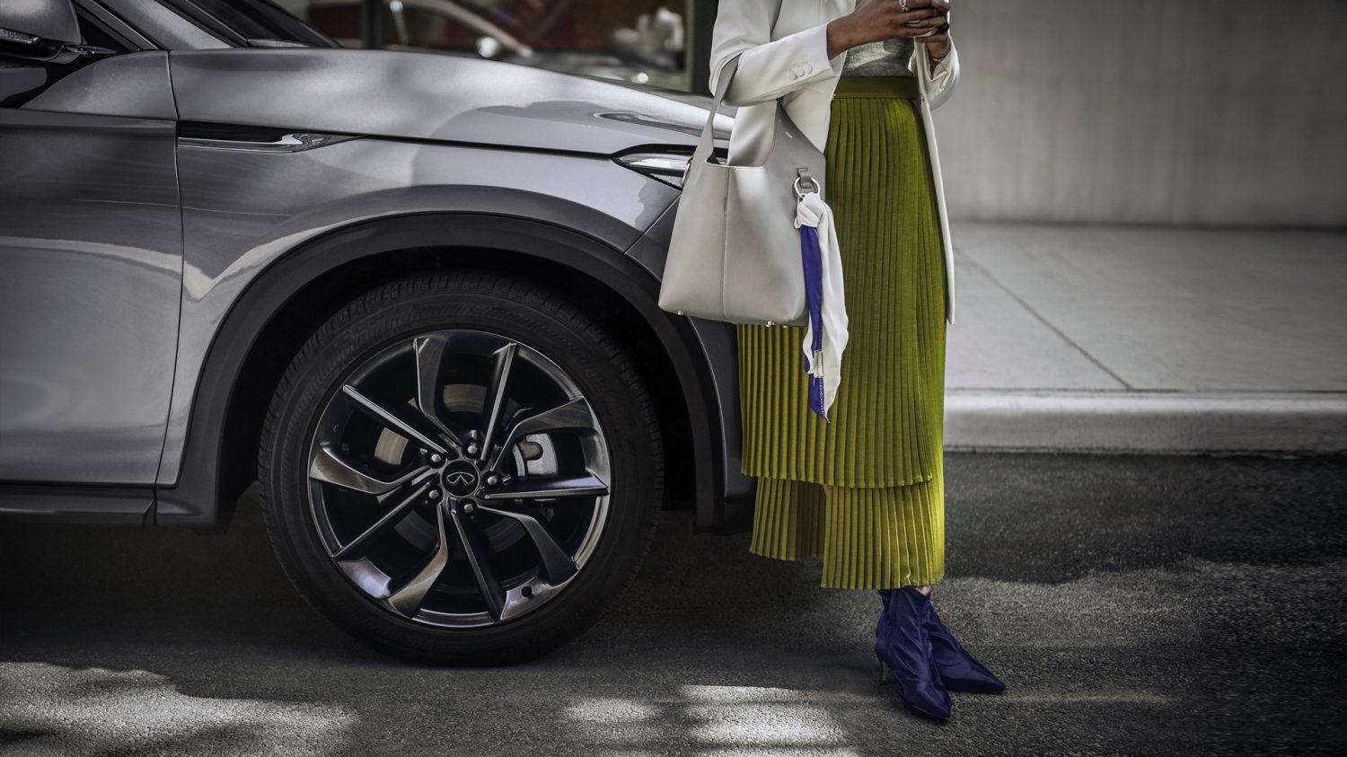 Mujer recargada en su QX50, esperando en la calle
